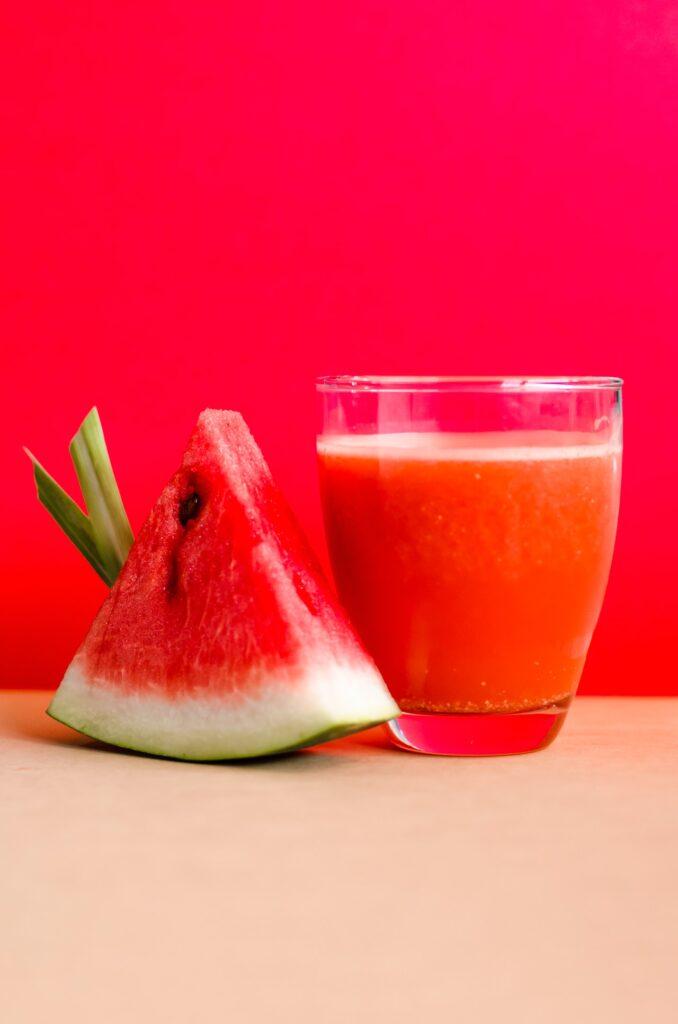 watermelon slice next to a glass full of watermelon juice