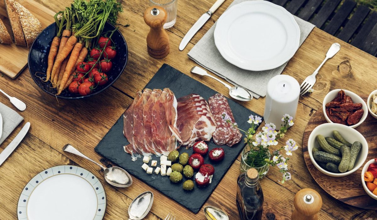 meats and vegetables on platters on a table with place settings