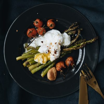 poached egg on top of asparagus on a black plate with silverware