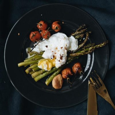 poached egg on top of asparagus on a black plate with silverware